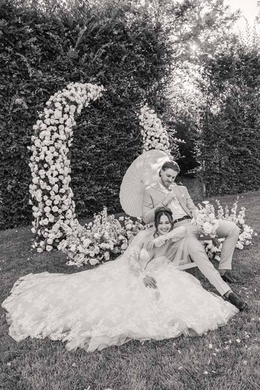 Lia-es-Doma-eskuvoi-fotozas-Daalarna Garden -432 Esküvői pár a természetben, virágos dekorációval és napernyővel.