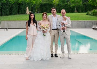 Esküvői kép a családról a medencénél, zöld park háttérrel.