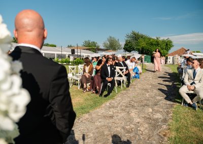 Esküvői ceremónia szabadban, vendégek és menyasszonyi ruha a háttérben.