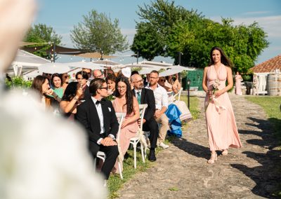 Esküvői vendégek és menyasszonyi koszorúslány a szabadban, napfényes napon.