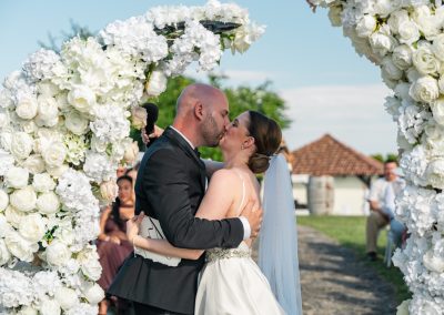 Esküvői pár csók az esküvői szertartás alatt, virágos kapu előtt.