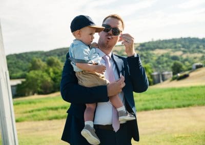 Esküvői kép egy férfi és egy kisfiú a természetben, napfényes napon.