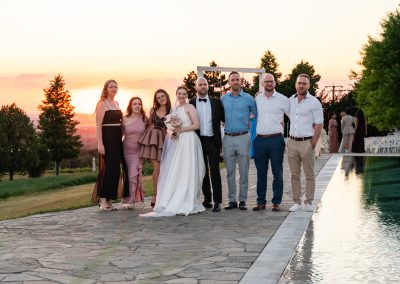 Esküvői csoportkép a naplementében, romantikus hangulatban.