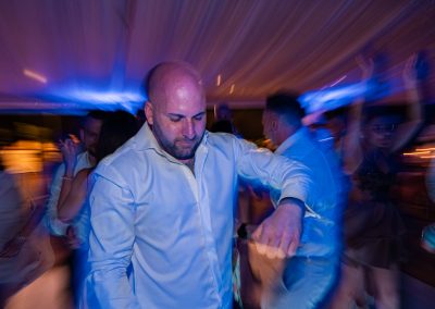 Esküvői férfi táncol a násznép között, dinamikus mozdulatokkal és színes fényekkel körülvéve.