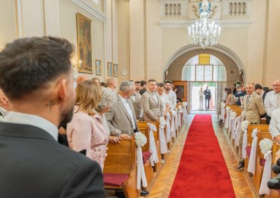 Esküvői ceremónia a templomban, vendégek és pár a háttérben.