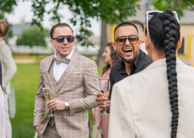 Esküvői vendégek nevetnek és beszélgetnek a szabadban, elegáns ruhában.